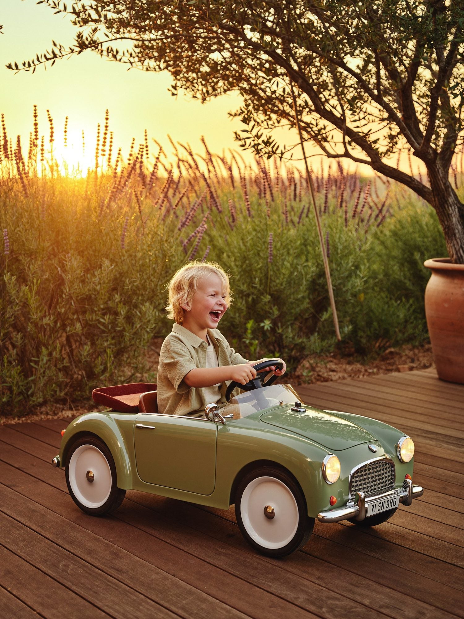 Enfant riant au volant d'une petite voiture verte dans un champ de lavande au coucher du soleil